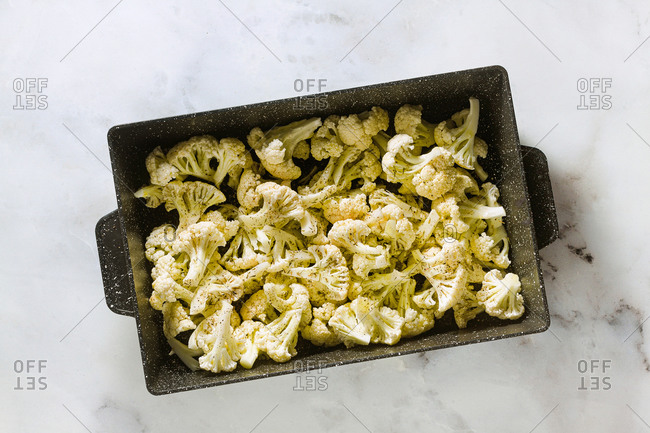 Slices of cauliflower in a baking tray with olive oil, aromatic herbs and spices, ready for baking on the marble table, copy space.