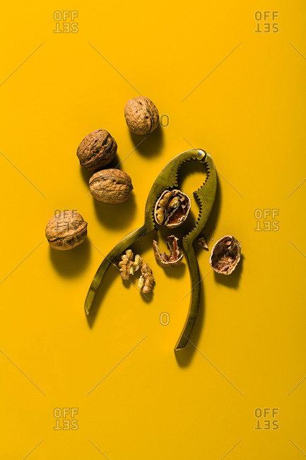 Nut set from natural organic walnuts and metal nutcracker on a yellow background with soft shadows and copy space. Top view.