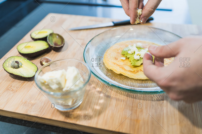 Man cooking in the kitchen in a denim shirt. An anonymous man is cooking pancakes with feta cheese and avocado