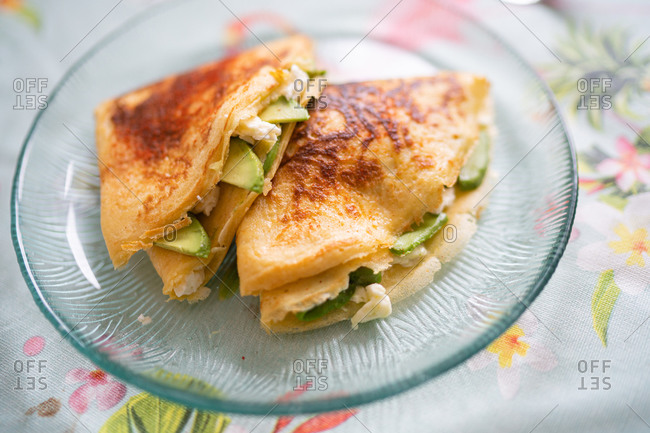 A plate of pancakes with cheese and avocado is on the table with a colorful tablecloth