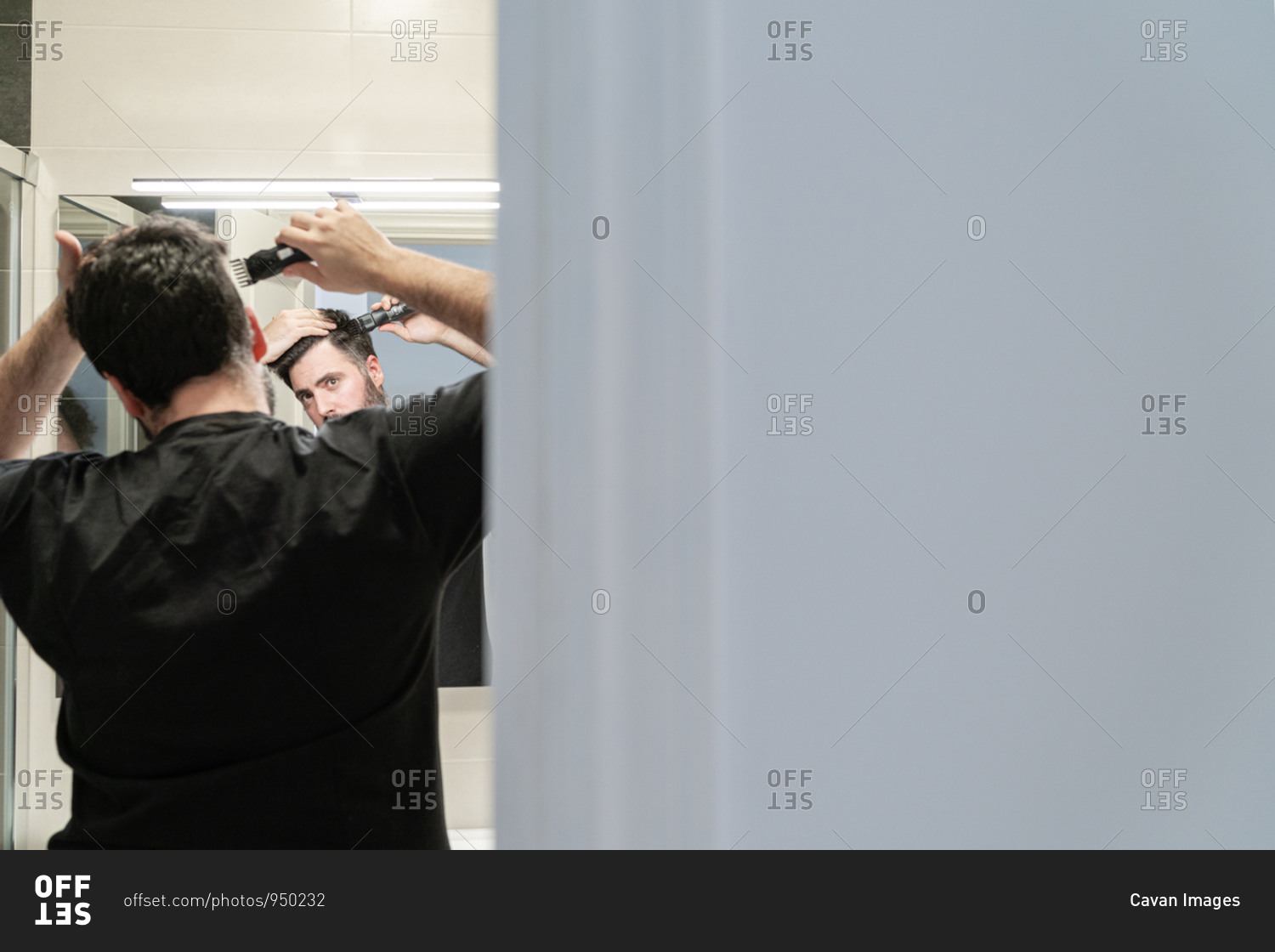 Self haircut. A man is cutting his hair with a hair clipper in the bathroom