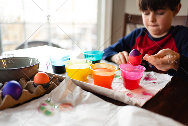 Boy dipping an egg into a bowl of dye to color it for Easter.