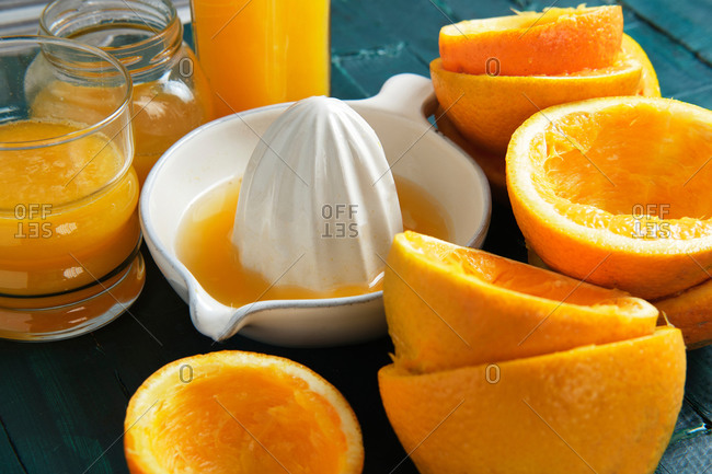 White ceramic juicer with orange peels and orange juice on a green wooden background