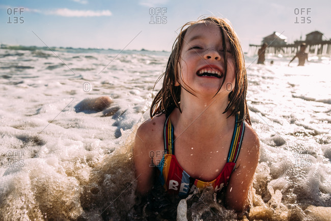 Young girl playing laying on beach while a wave crashes on her