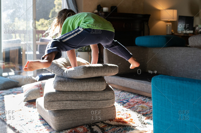 Child jumping over a pile of couch cushion pillows in living room