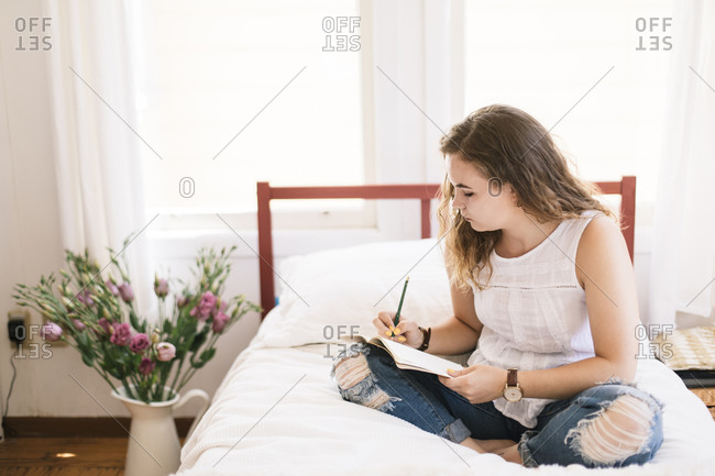 High School girl writing on journal while in bed by fresh flowers