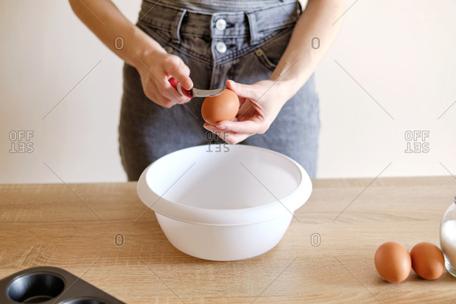 Woman breaks an egg with a knife over a plate to cook a delicious meal