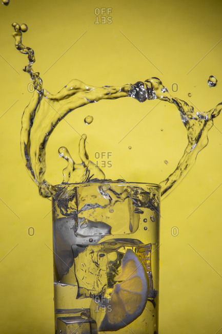 Splashing cocktail with lemon and ice on yellow background