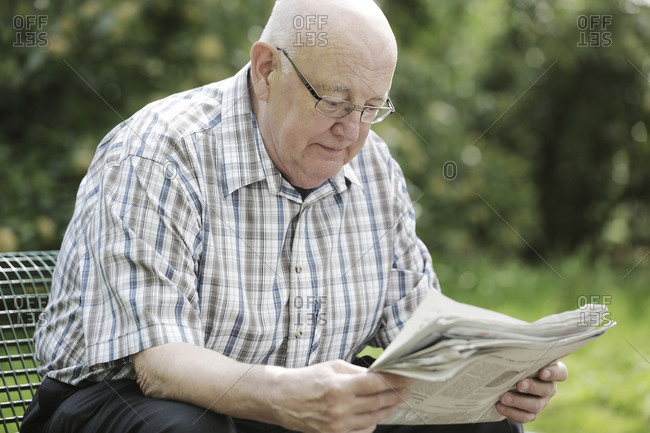 Germany- North Rhine Westphalia- Cologne- Senior man reading newspaper on bench in park