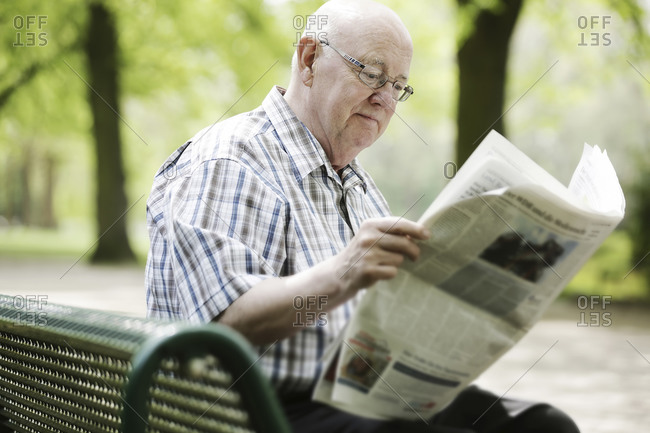 Germany- North Rhine Westphalia- Cologne- Senior man reading newspaper on bench in park