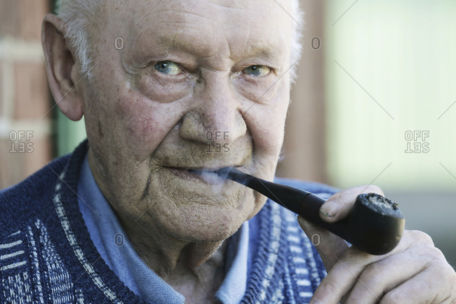 Germany- Portrait of senior man holding pipe- close up
