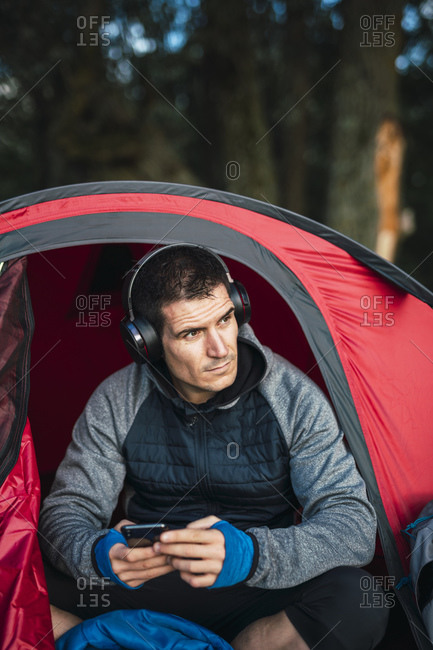 Man camping in Estonia- sitting in his tent- listening music from his smartphone