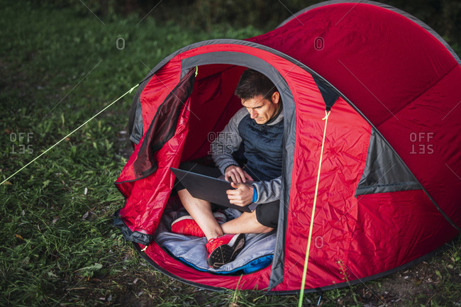 Man camping in Estonia- sitting in tent- using laptop