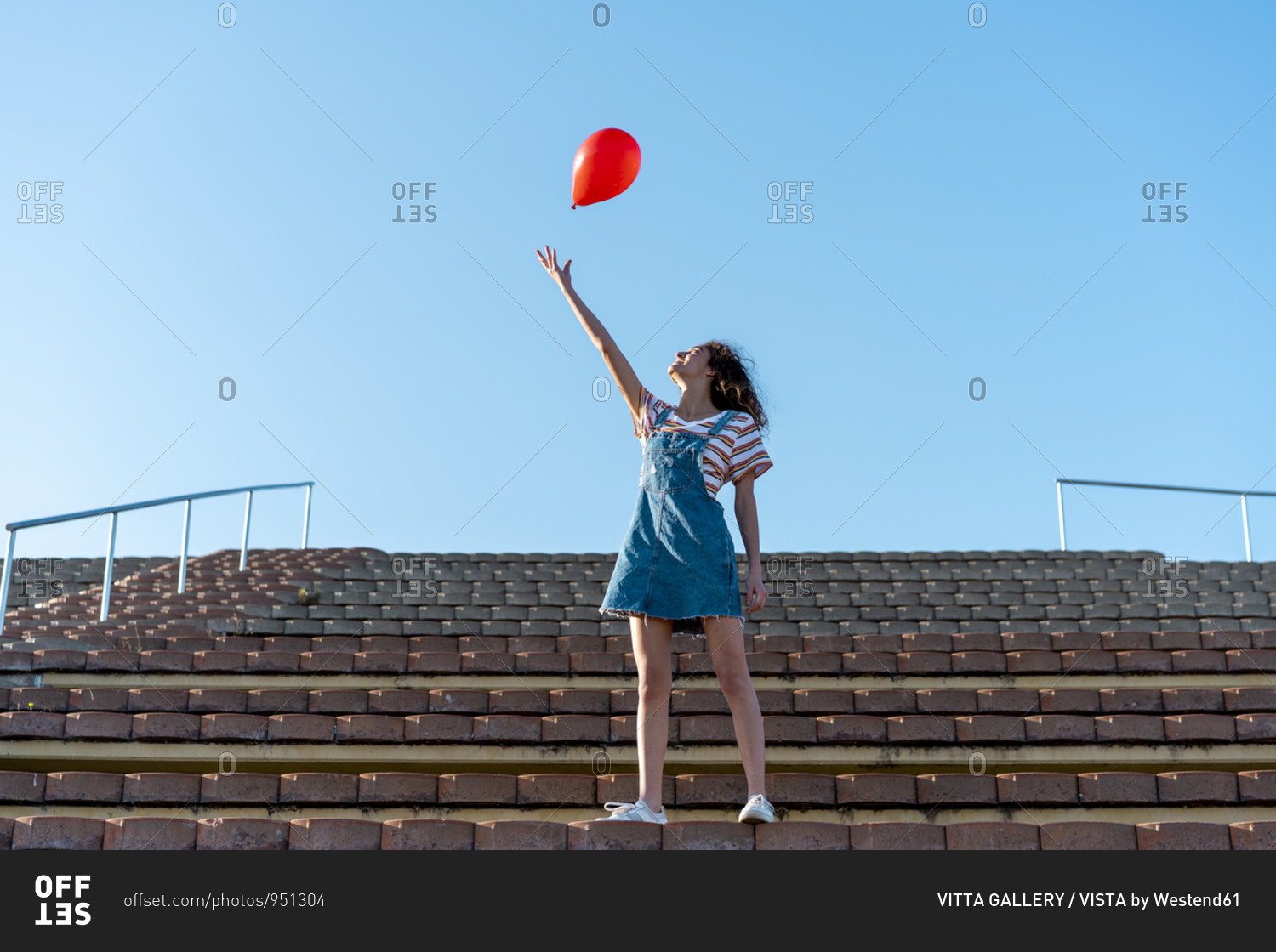 Young woman standing on grandstand- letting go of a red balloon