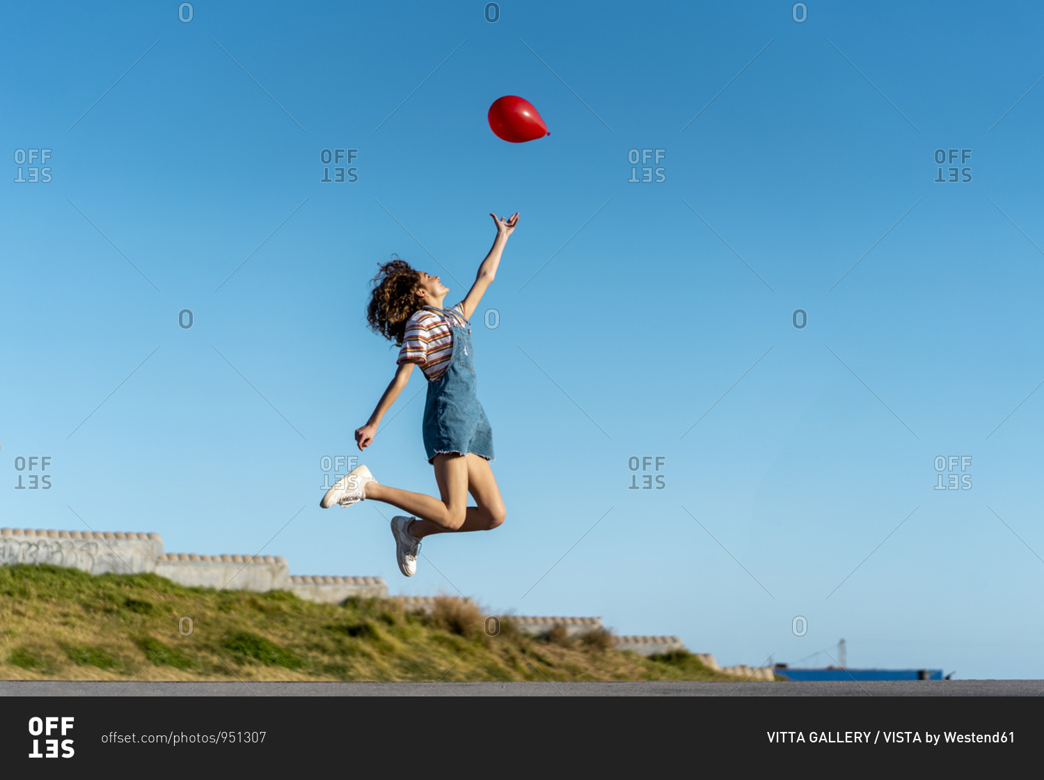 Jumping young woman- letting go of a red balloon