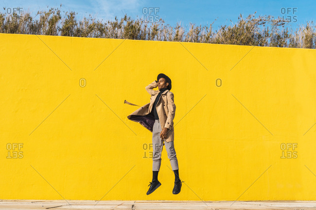 Young man dancing in front of yellow wall- jumping mid air