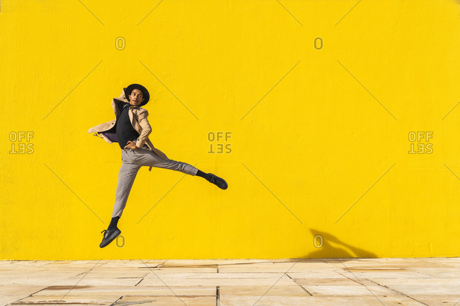 Young man dancing in front of yellow wall- jumping mid air