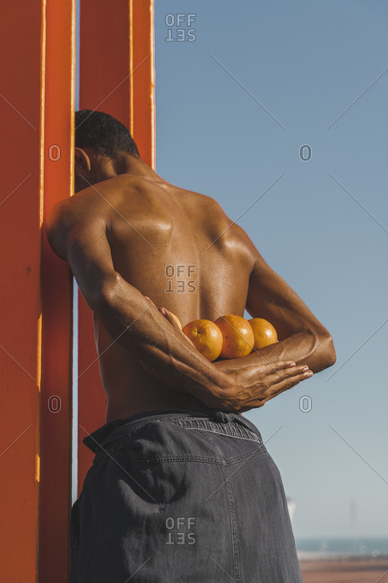 Bare-chested young man holding oranges outdoors