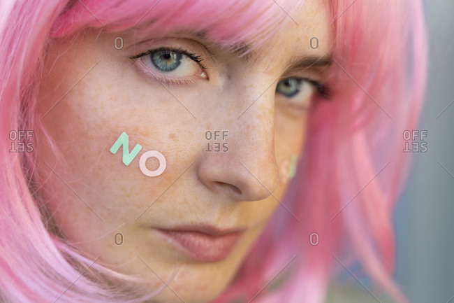 Portrait of young woman wearing pink wig with word 'no' on her cheek