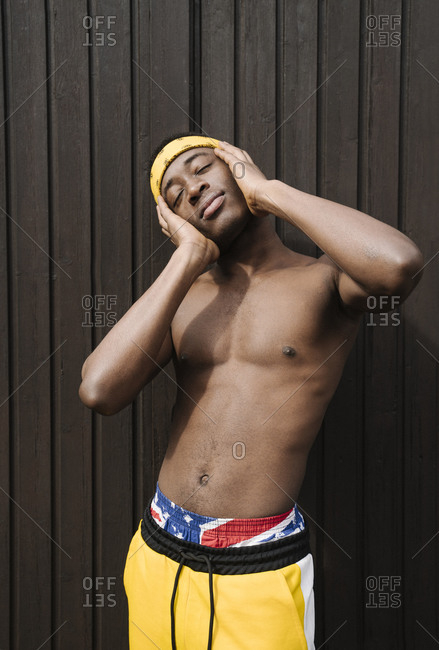 Portrait of shirtless man with eyes closed and hands on his face standing in front brown background