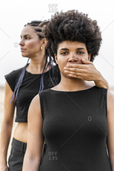 Woman's hand covering mouth of another woman