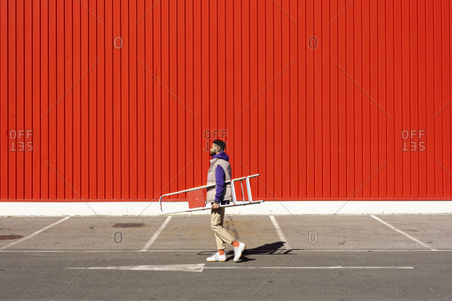 Young man carrying a ladder in front of a red wall