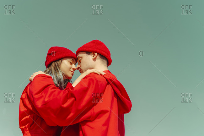Young couple wearing red overalls and hats standing head to head against sky