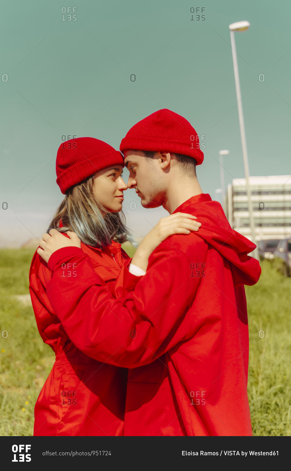 Young couple wearing red overalls and hats standing head to head looking at each other