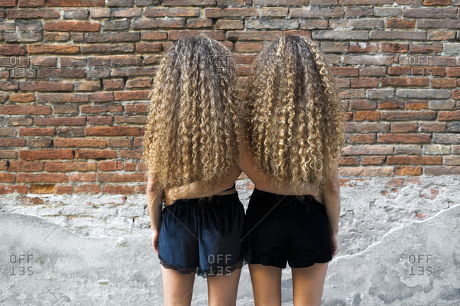 Back view of twin sisters with ringlets standing arm in arm side by side