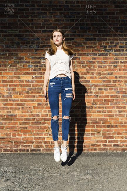 Agile young woman jumping in front of brick wall