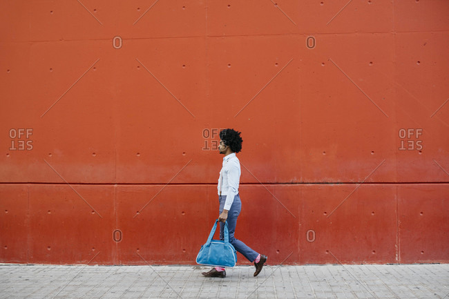 Man with bag walking down the street in front of a red wall