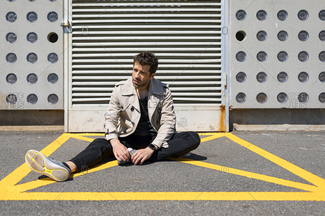 Helpless man sitting on ground in yellow marked area in front of concrete wall