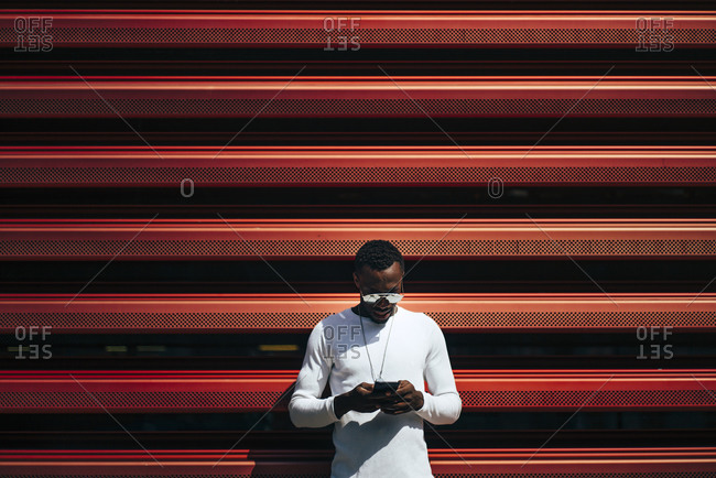 Young man using mobile phone at a red wall
