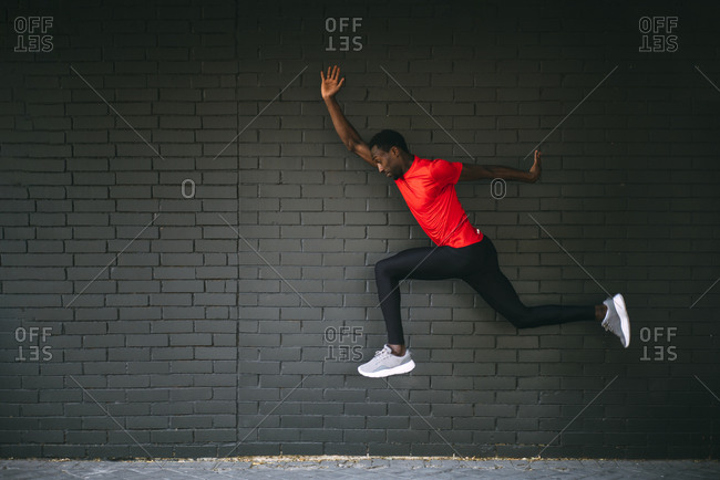 Young sportive man jumping in front of a brick wall
