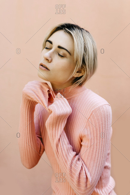 Portrait of young woman with closed eyes wearing pink turtleneck pullover in front of a pink wall