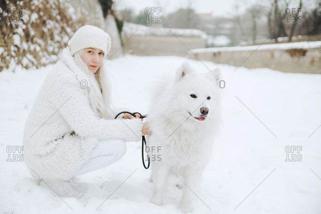 Portrait of white dressed young woman with white dog in the snow
