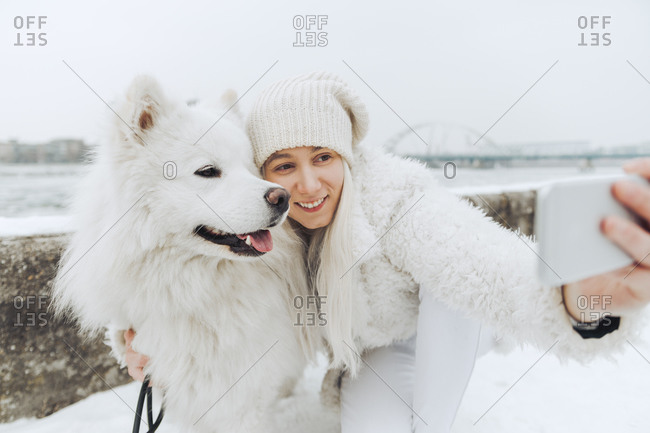 White dressed woman taking selfie with her white dog in winter