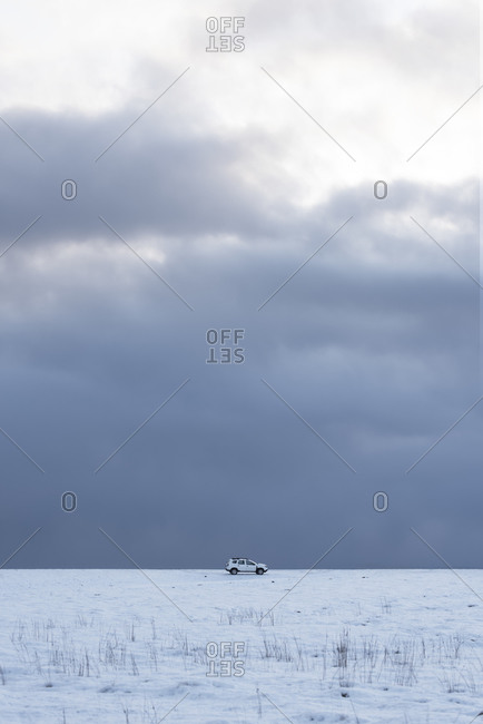 Cold winter landscape with snowy white terrain with white car and remote lonely traveler against backdrop of endless delightful cloudy sky in cold winter