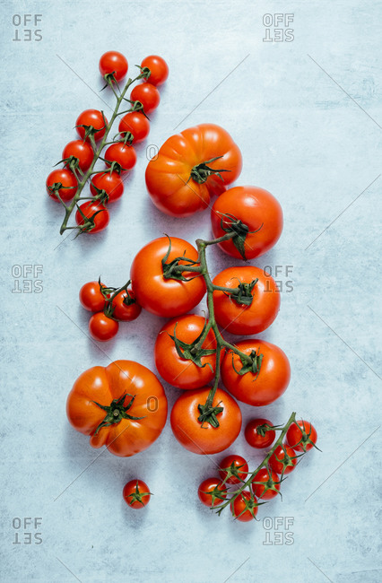 Top view of whole big and small cherry red tomatoes on green stems on light blue table in modern kitchen in sunbeams