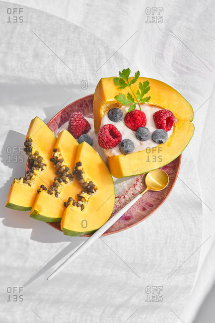 From above pieces of ripe papaya with yoghurt and fresh berries placed near spoon on plate on white background