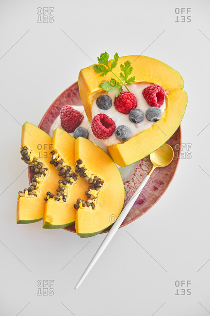 From above pieces of ripe papaya with yoghurt and fresh berries placed near spoon on plate on white background