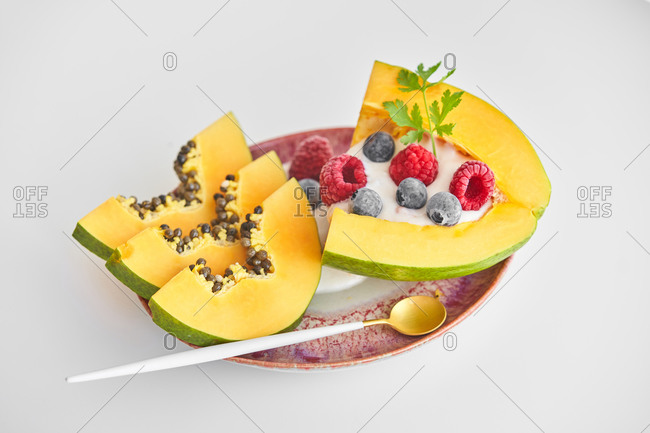 From above pieces of ripe papaya with yoghurt and fresh berries placed near spoon on plate on white background