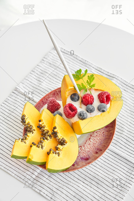From above pieces of ripe papaya with yoghurt and fresh berries placed near spoon on plate on white background