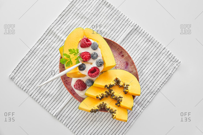 From above pieces of ripe papaya with yoghurt and fresh berries placed near spoon on plate on white background