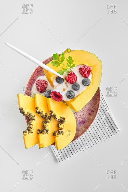 From above pieces of ripe papaya with yoghurt and fresh berries placed near spoon on plate on white background