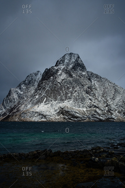Breathtaking view of blue rippled sea water against snowy mountain ridges on shore under gray cloudy sky in wintertime in Norway