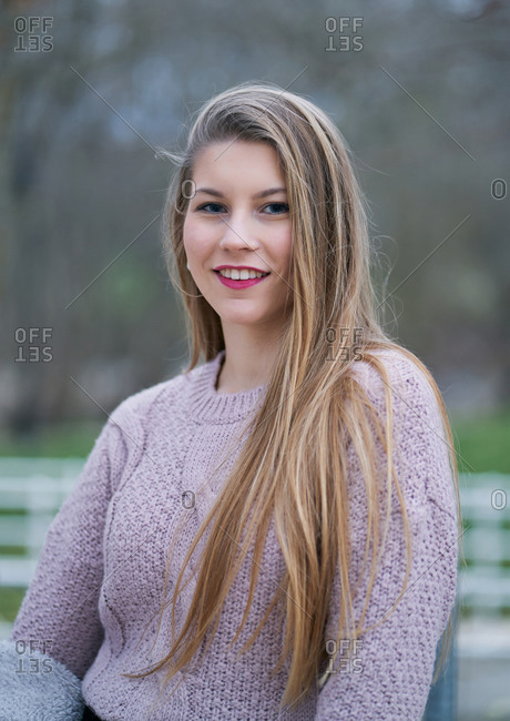 Blond woman wearing light purple sweater and smiling at camera against blurry background