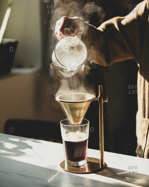 Woman pours coffee into vintage brewer at kitchen
