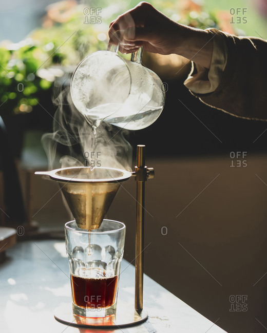 Woman pours coffee into vintage brewer at kitchen