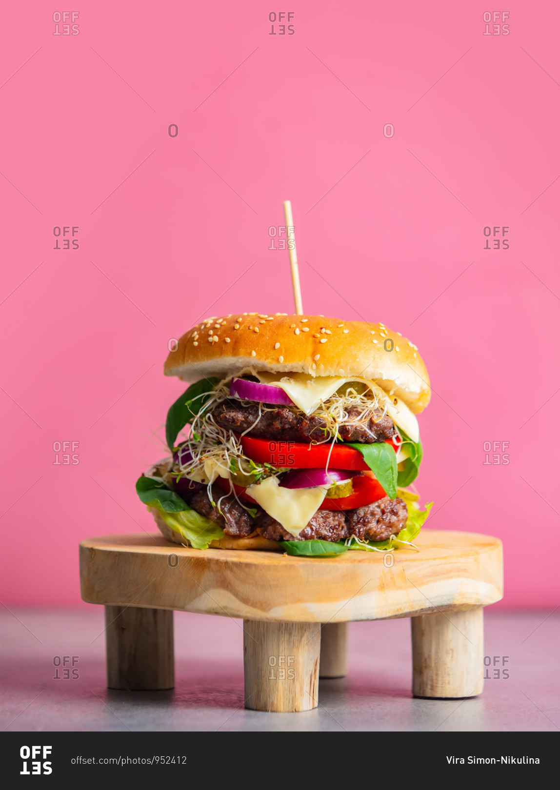 Home-made burger with meat and cheese on stand on pink background